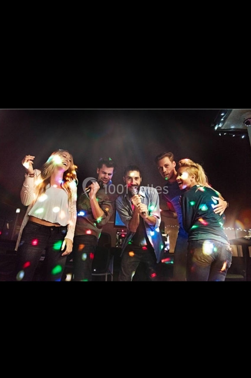 Des personnes chantent et dansent sous des lumières colorées dans une ambiance festive en intérieur.