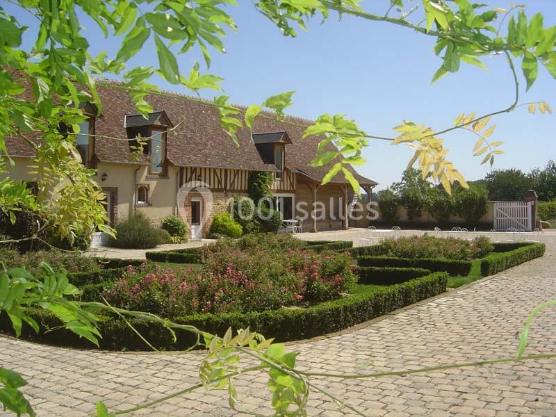 Jardin paysager avec haies taillées et rosiers devant une maison à colombages sous un ciel dégagé.
