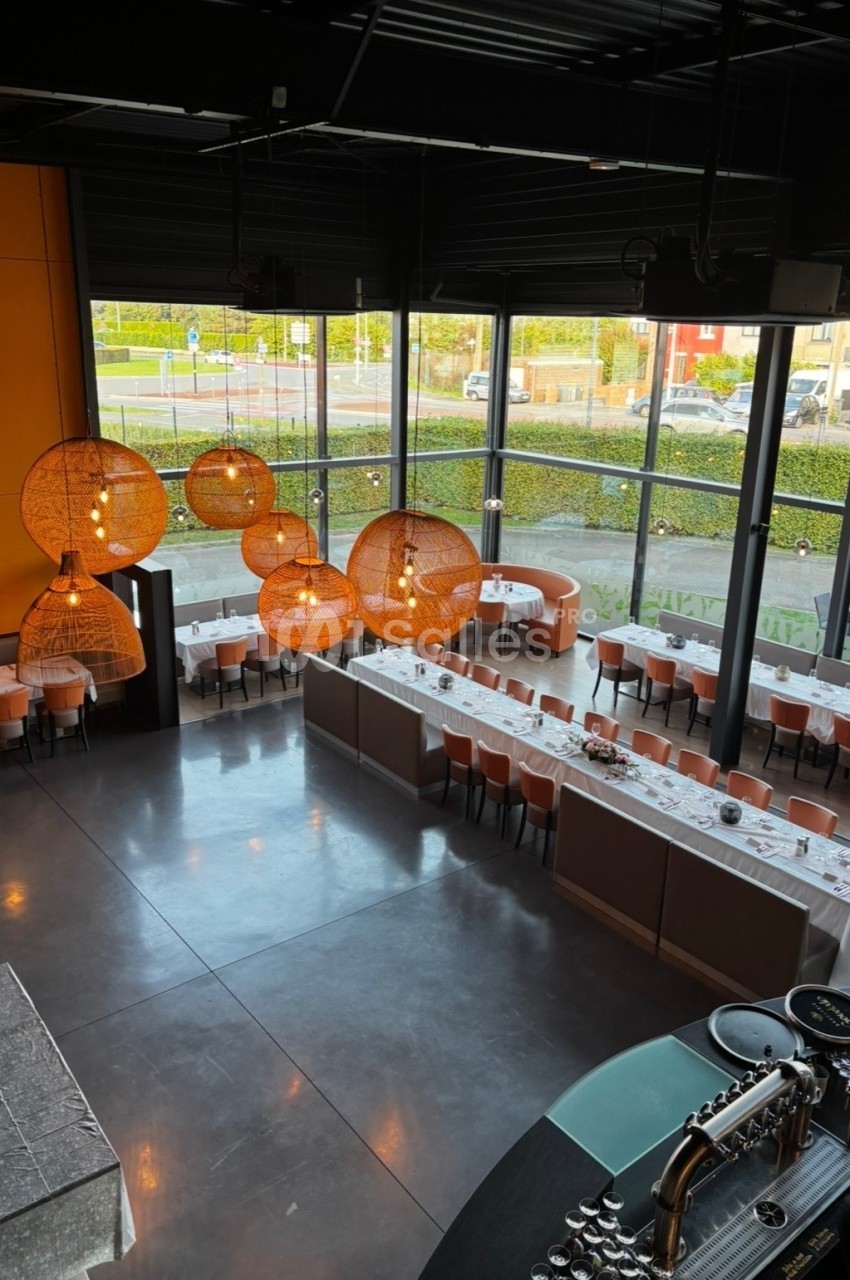 Vue d'un restaurant moderne avec de grandes baies vitrées, des tables dressées et des luminaires suspendus en osier.