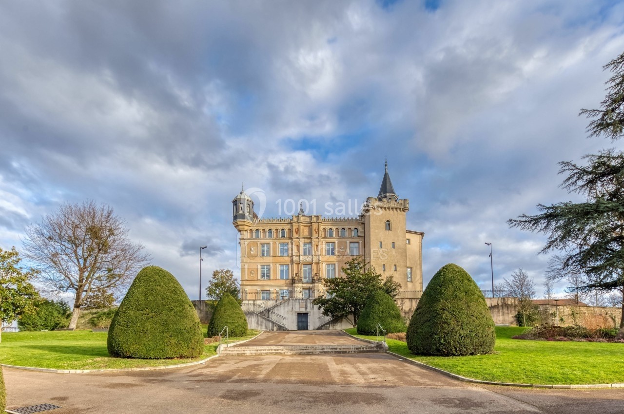 Façade d'un château historique entouré de jardins bien entretenus, sous un ciel partiellement nuageux.