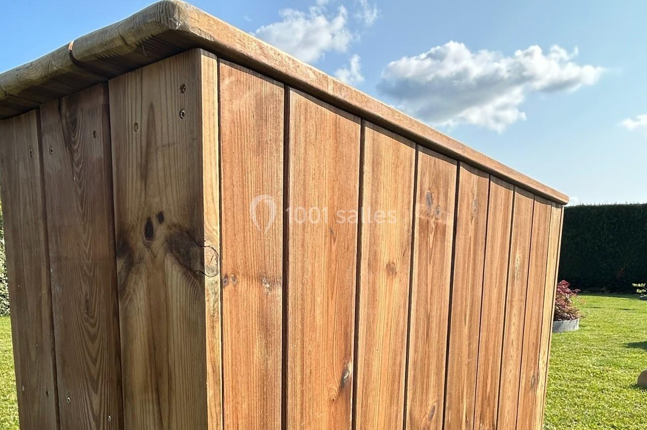 Vue rapprochée d'un coffre en bois avec des panneaux verticaux, placé dans un jardin ensoleillé.