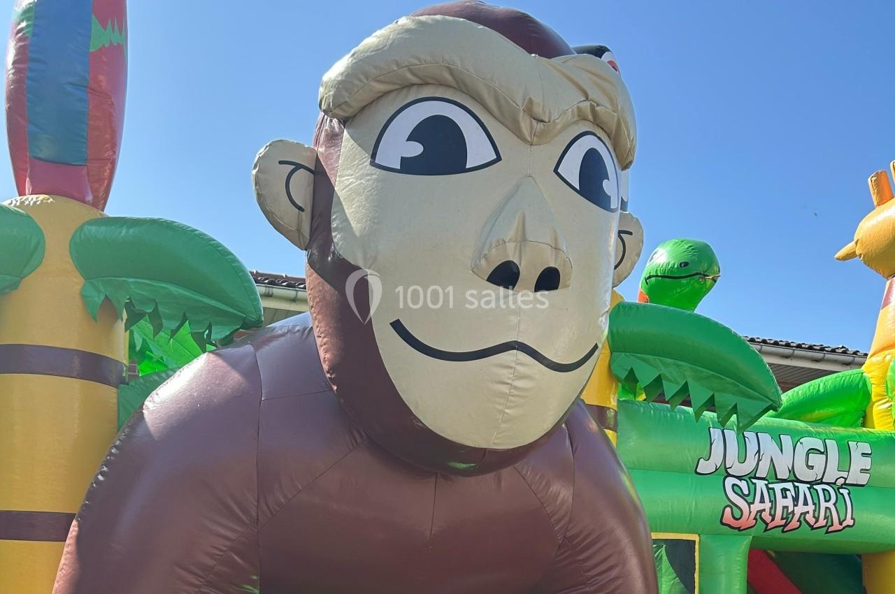 Structure gonflable en forme de singe entourée de décorations sur le thème de la jungle sous un ciel bleu.