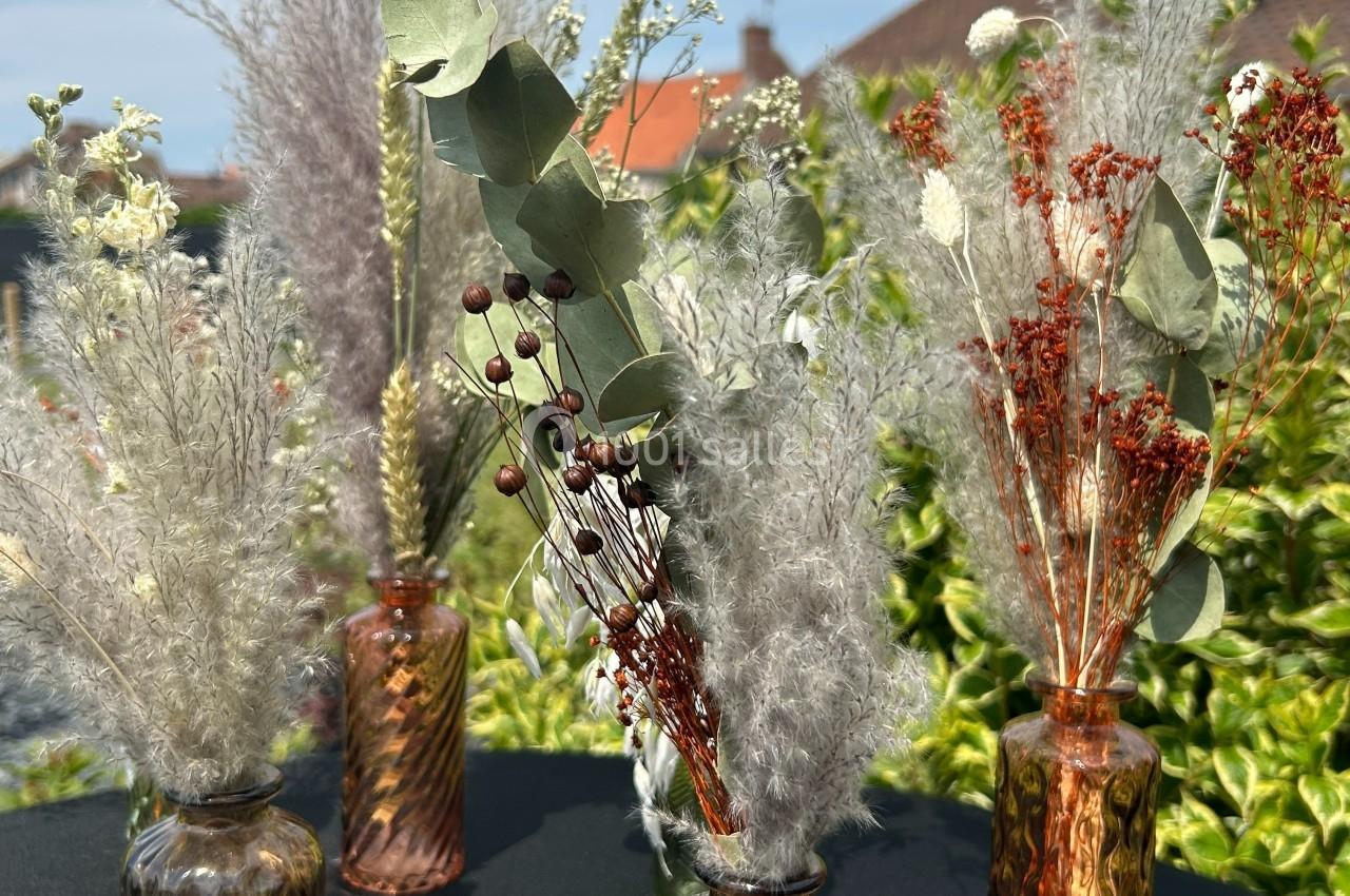 Bouquets de fleurs séchées variées disposés dans des vases en verre marron, avec un fond de jardin verdoyant.