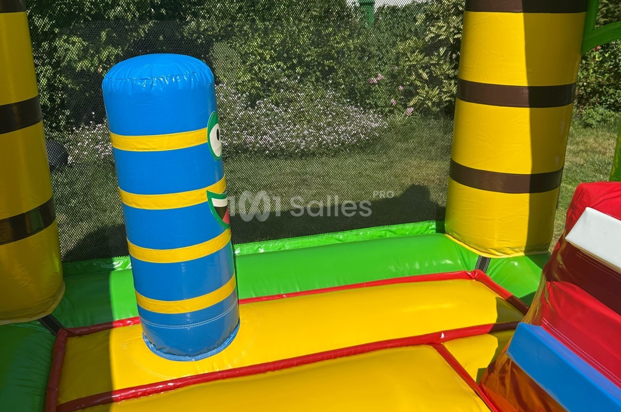 Structure gonflable colorée avec un obstacle cylindrique bleu et jaune, située dans un jardin verdoyant.