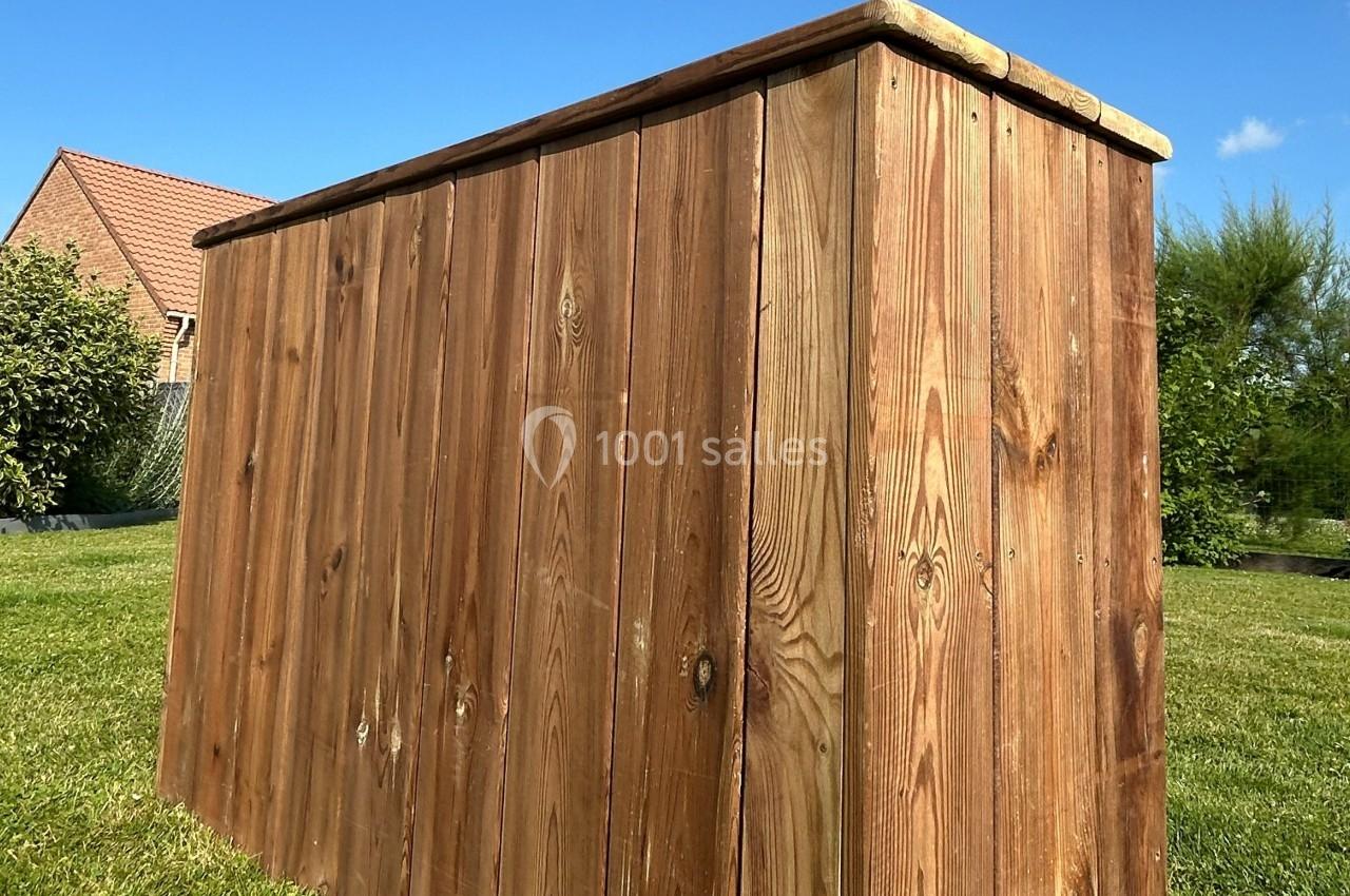 Coffre de rangement en bois sur une pelouse, avec une maison et des arbres en arrière-plan.