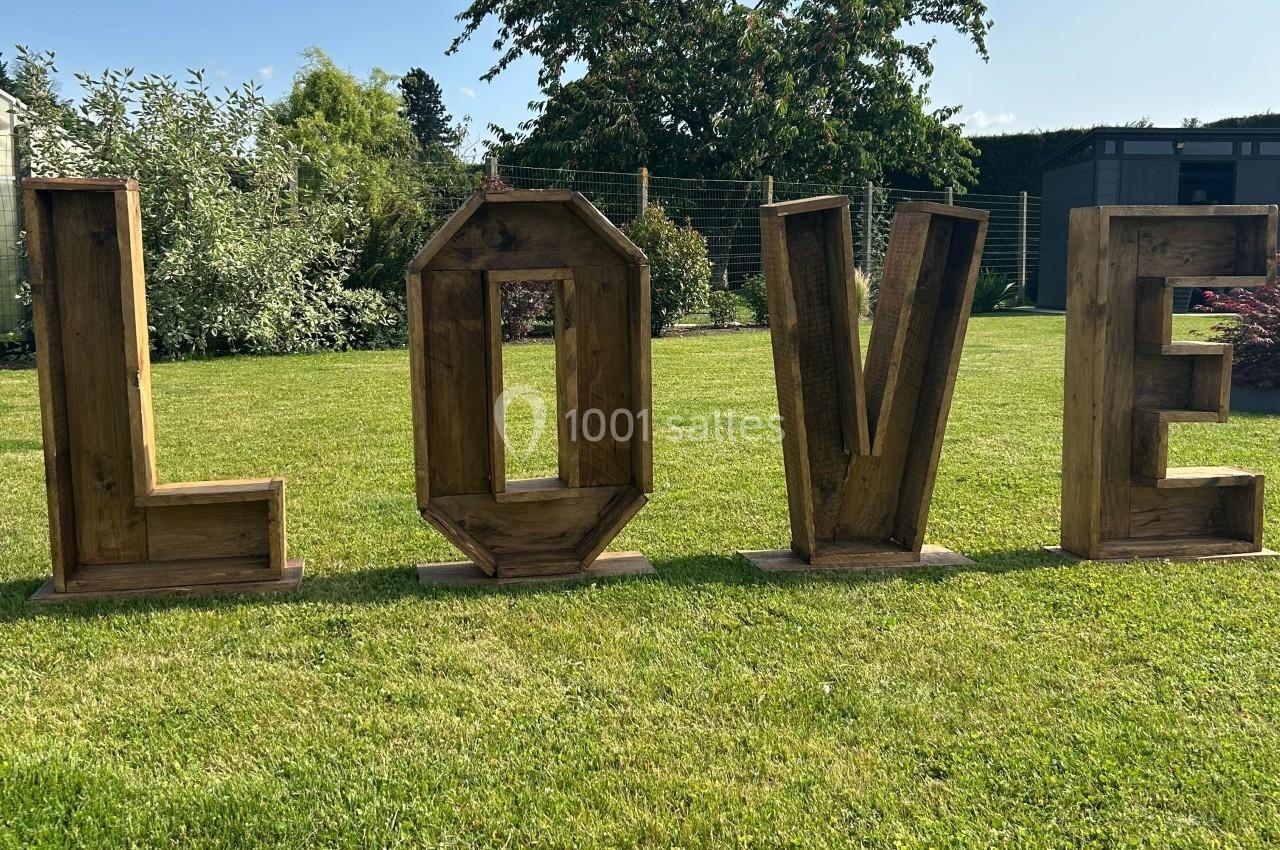 Lettres en bois formant le mot ’LOVE’ disposées sur une pelouse, avec des arbres et une clôture en arrière-plan.