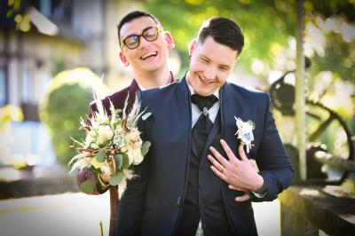 Miniature Victor Podgorski Photographe #8 Un couple en tenue de mariage s'embrasse dans un champ de blé, tenant des ballons colorés sous un ciel bleu.