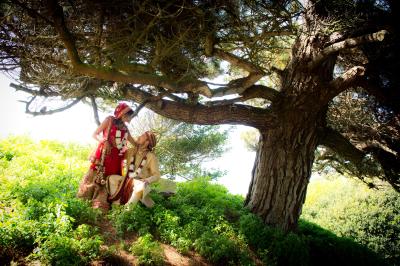 Miniature Victor Podgorski Photographe #9 Un couple en tenue de mariage s'embrasse dans un champ de blé, tenant des ballons colorés sous un ciel bleu.