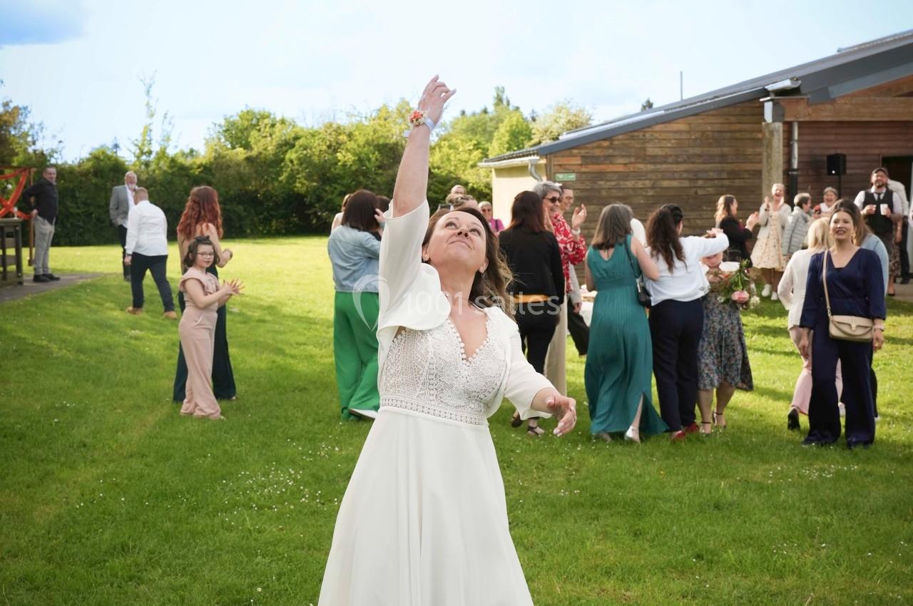 Une mariée lance son bouquet de fleurs dans un jardin, entourée d'invités lors d'une réception en plein air.