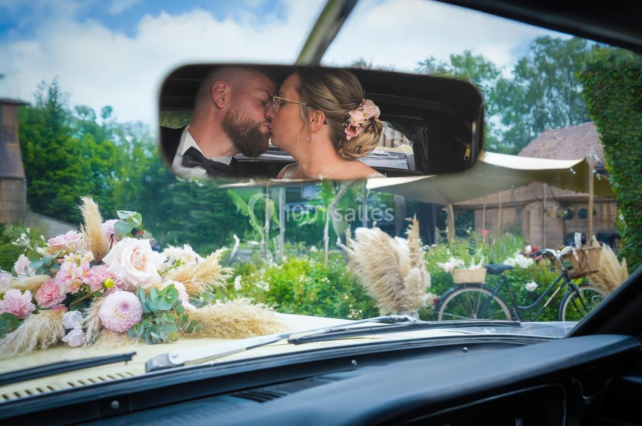 Un couple s'embrasse dans le rétroviseur d'une voiture décorée de fleurs, avec un jardin en arrière-plan.