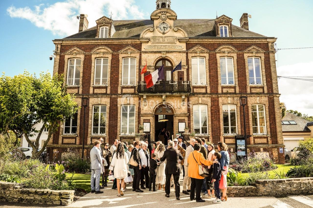 Groupe de personnes rassemblées devant une mairie en briques rouges par une journée ensoleillée.