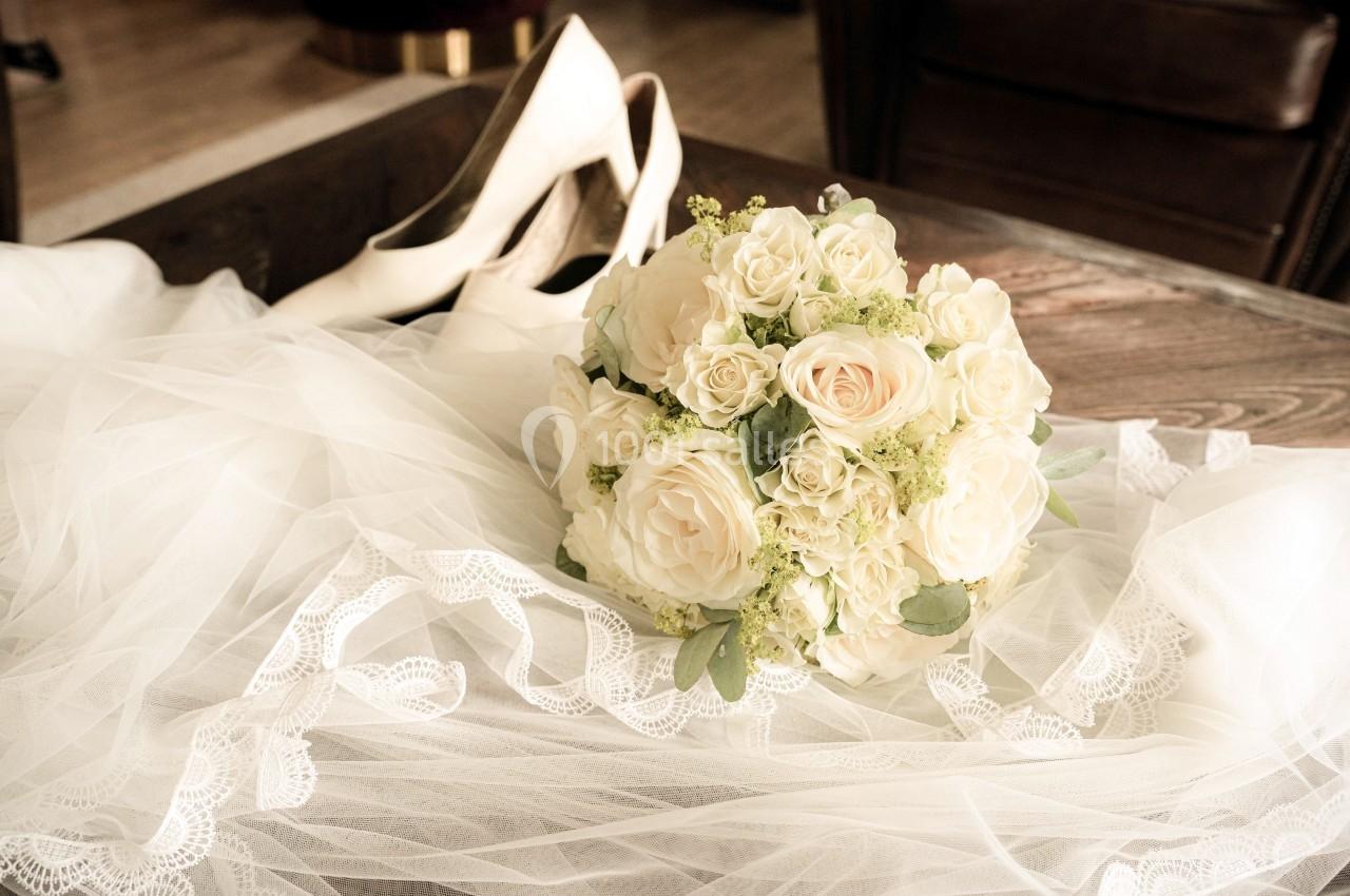 Bouquet de roses blanches posé sur un voile en dentelle, avec des chaussures de mariée en arrière-plan.