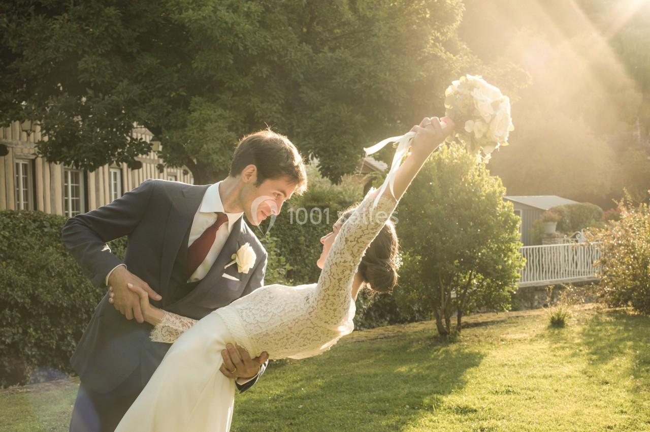 Un couple en tenue de mariage danse dans un jardin baigné par une lumière dorée.