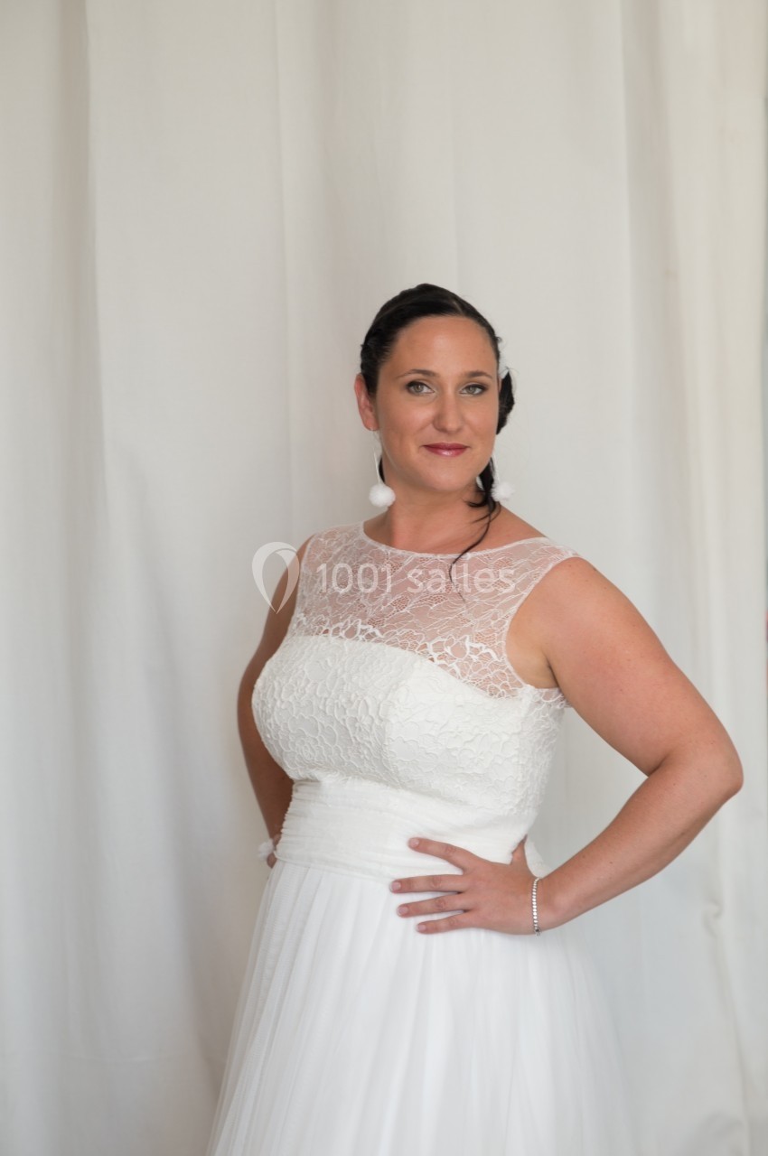 Femme en robe de mariée blanche avec un haut en dentelle, posant devant un fond clair.