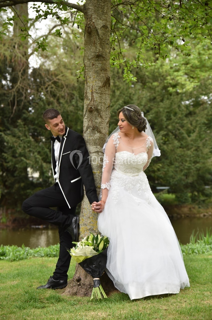 Un couple de mariés pose près d'un arbre dans un parc, se tenant la main sans se regarder.