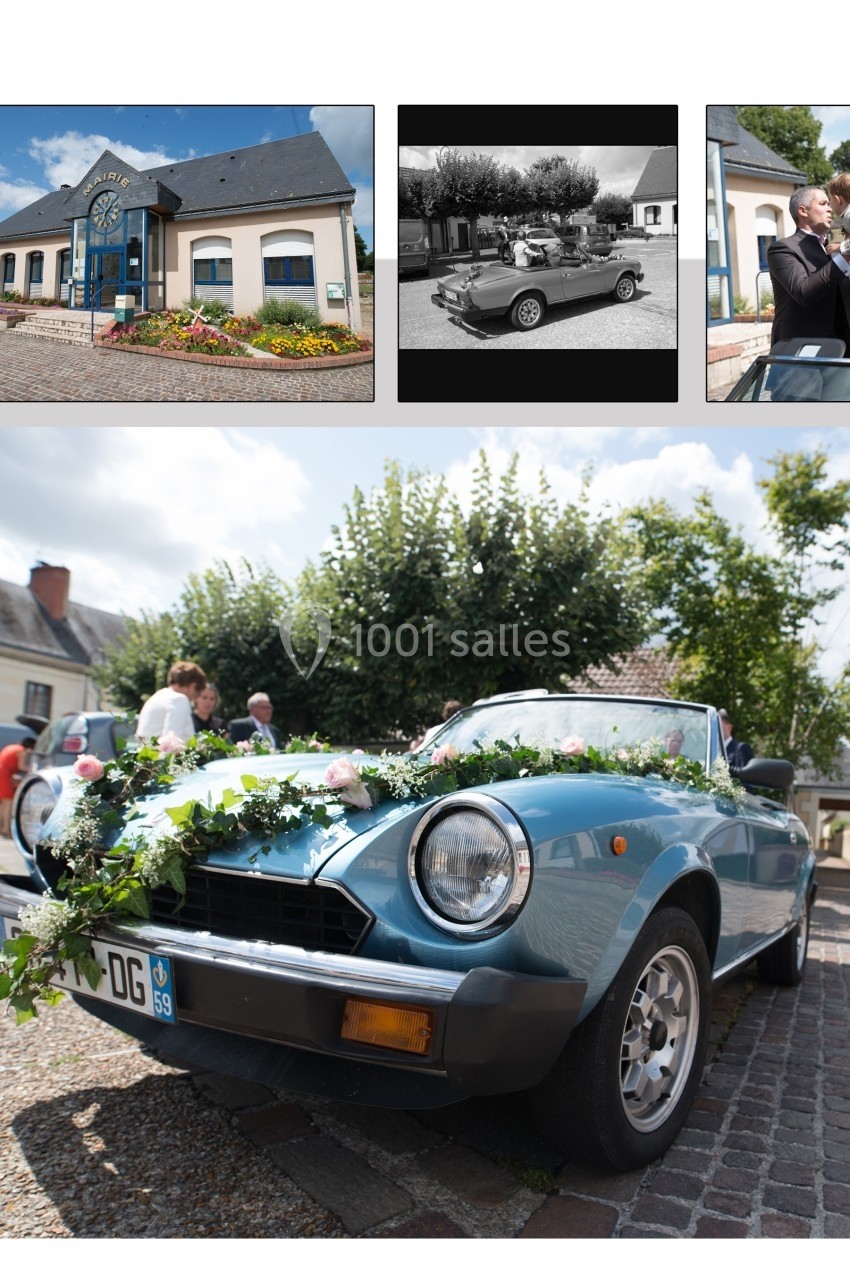 Voiture ancienne décapotable bleue décorée de fleurs, stationnée sur une place pavée devant des bâtiments.