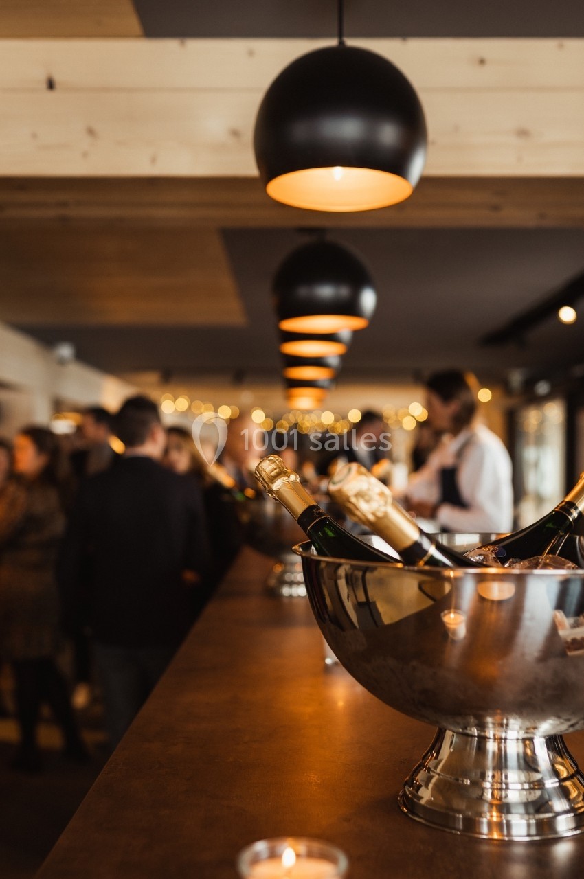 Des bouteilles de champagne dans un seau en métal sur un comptoir, avec des personnes en arrière-plan dans un bar.