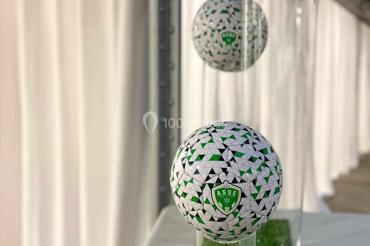 Trois ballons de football décoratifs aux motifs verts et blancs, posés sur des vases en verre sur une table.