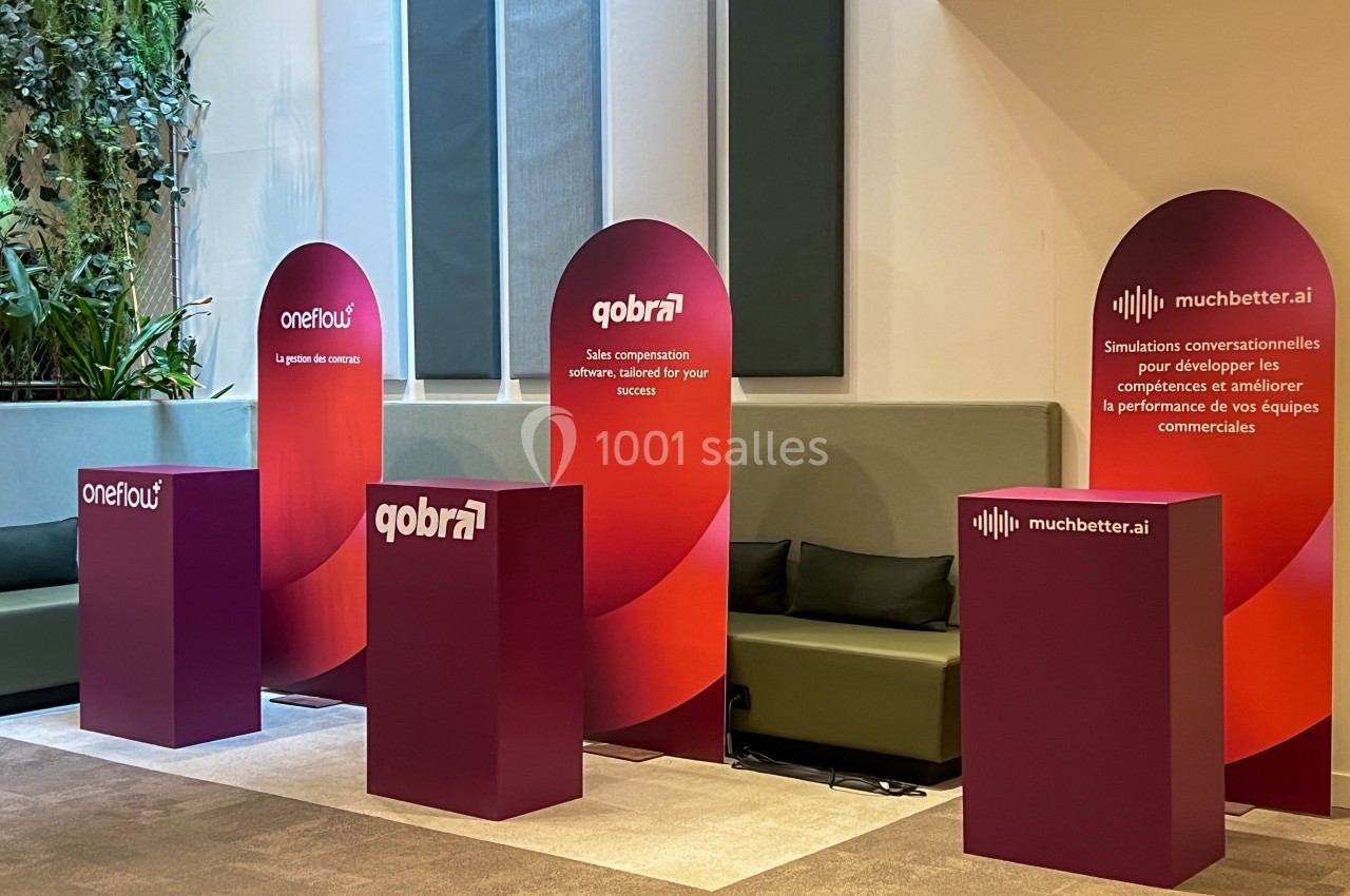 Trois stands promotionnels avec panneaux rouges et logos d'entreprises, disposés devant des banquettes dans un espace…