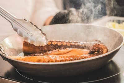 Miniature Traiteur Boulogne-Billancourt (Hauts-de-Seine) - Bellota Bellota #15 Tentacules de poulpe en train de cuire dans une poêle, manipulés avec une pince en métal.