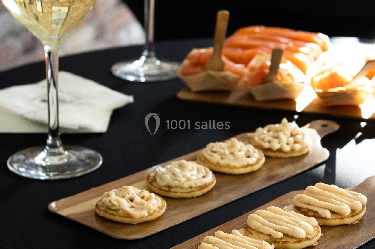 Assortiment de canapés au saumon et à la crème disposés sur des planches en bois, avec un verre de vin blanc.