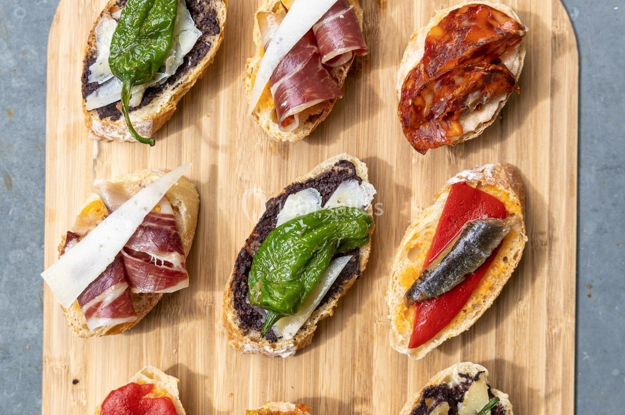 Assortiment de tapas sur une planche en bois, comprenant charcuterie, légumes grillés et fromage.