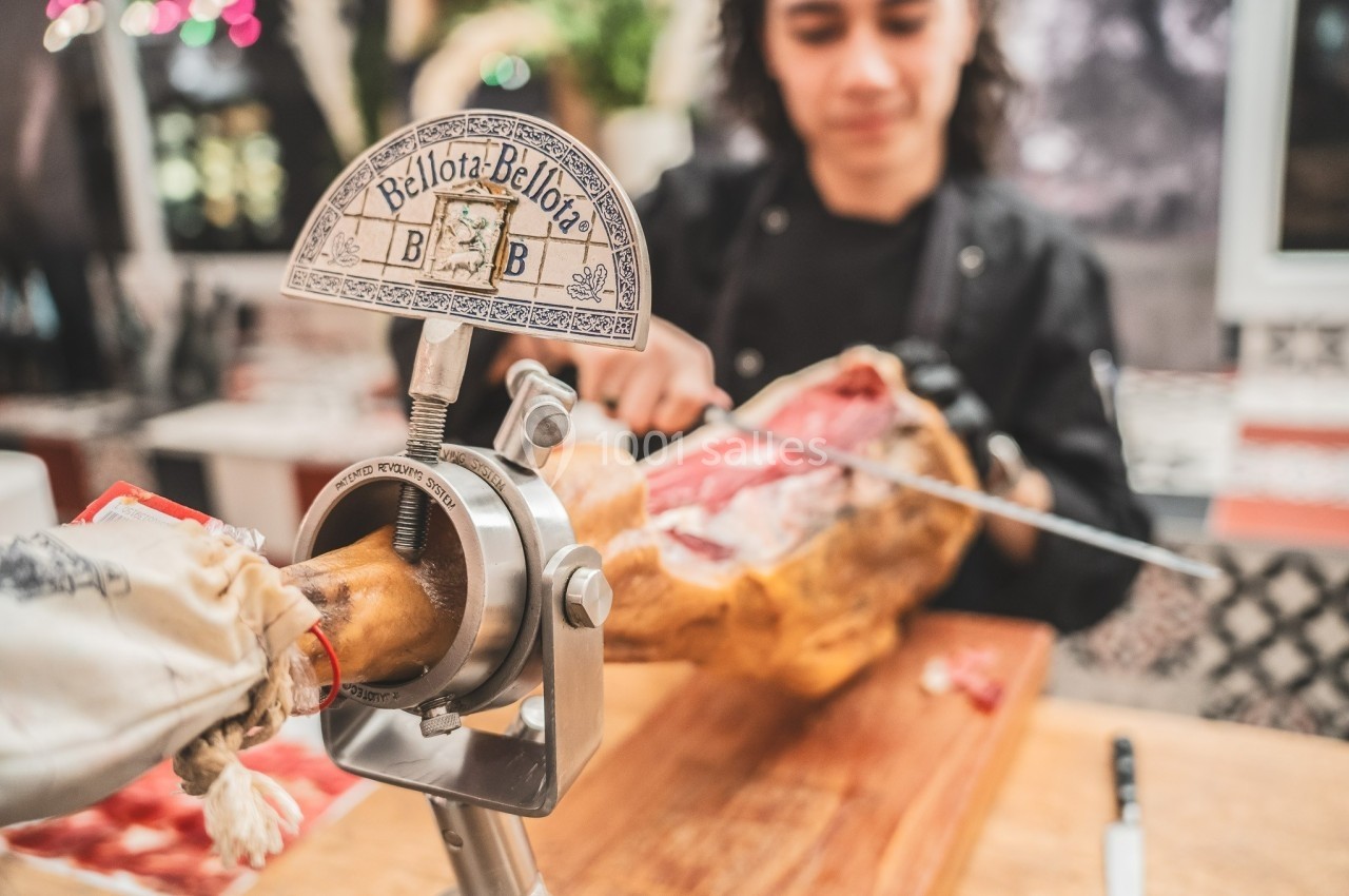 Personne découpant une tranche de jambon serrano fixé sur un support dans un environnement de cuisine.