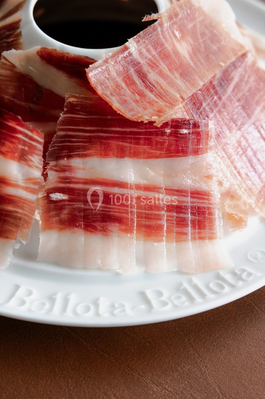 Tranches fines de jambon ibérique disposées en cercle sur une assiette blanche.