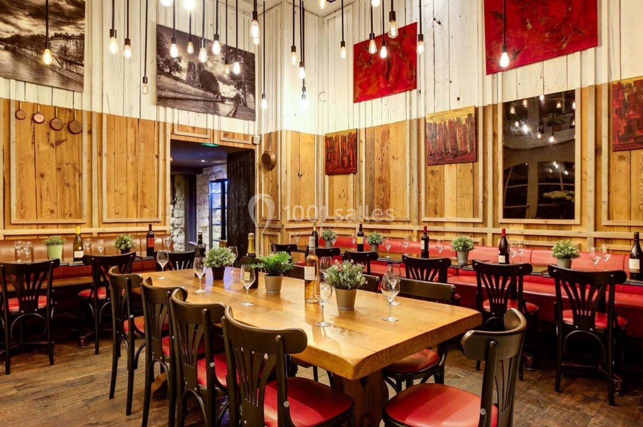 Salle de restaurant chaleureuse avec tables en bois, chaises noires, décorations murales et éclairage suspendu.