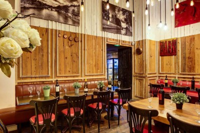 Salle de restaurant avec tables alignées, chaises noires, bouteilles de vin, plantes décoratives et murs en bois.