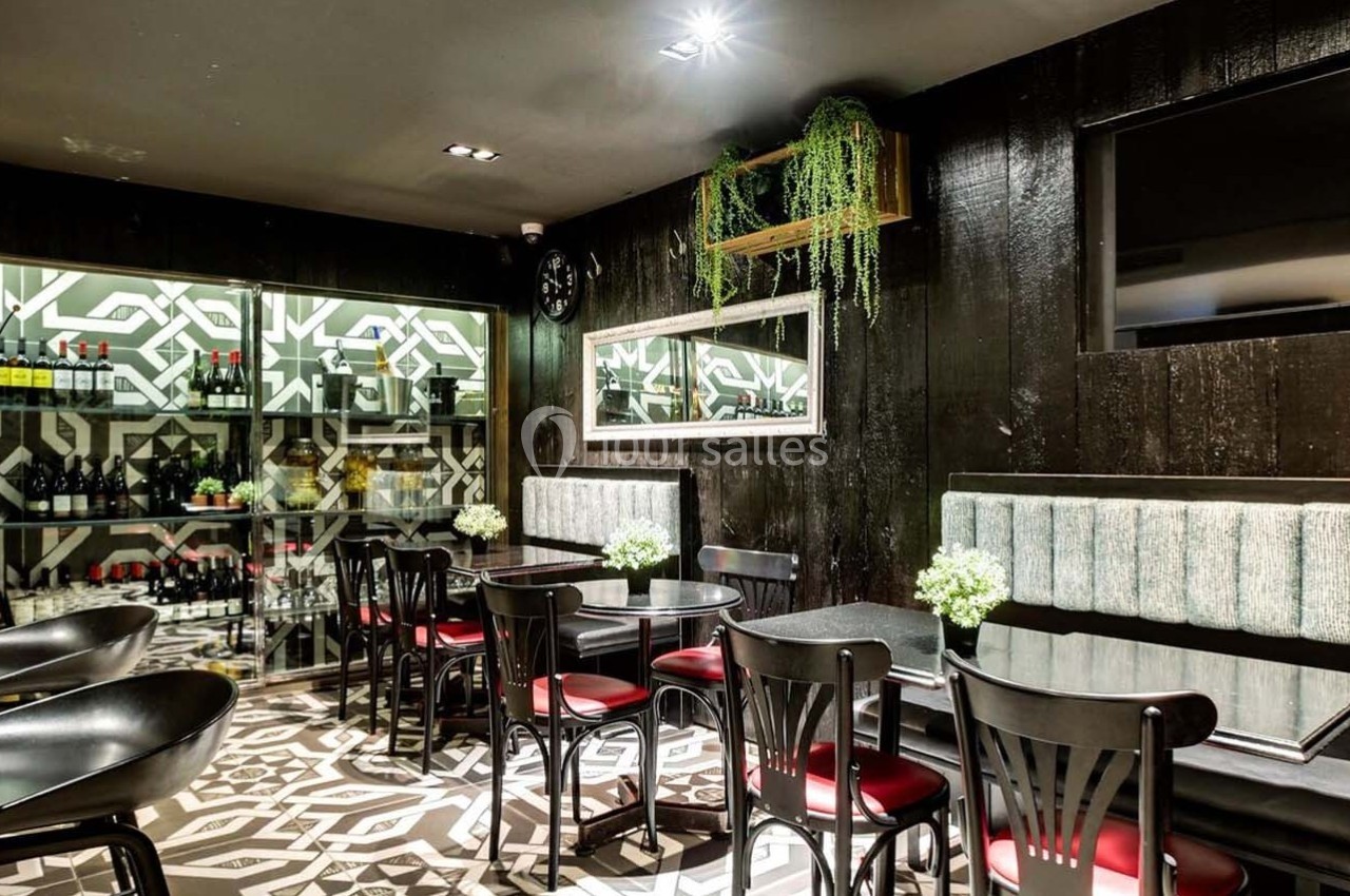 Salle de restaurant moderne avec tables noires, chaises rouges, banquettes grises et décoration végétale.