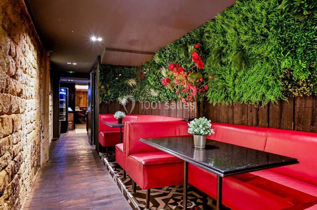 Banquettes rouges et tables noires alignées dans un espace avec mur en pierre et végétation murale.