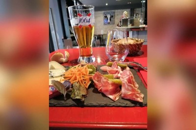 Salle de restaurant avec tables alignées, chaises noires, bouteilles de vin, plantes décoratives et murs en bois.