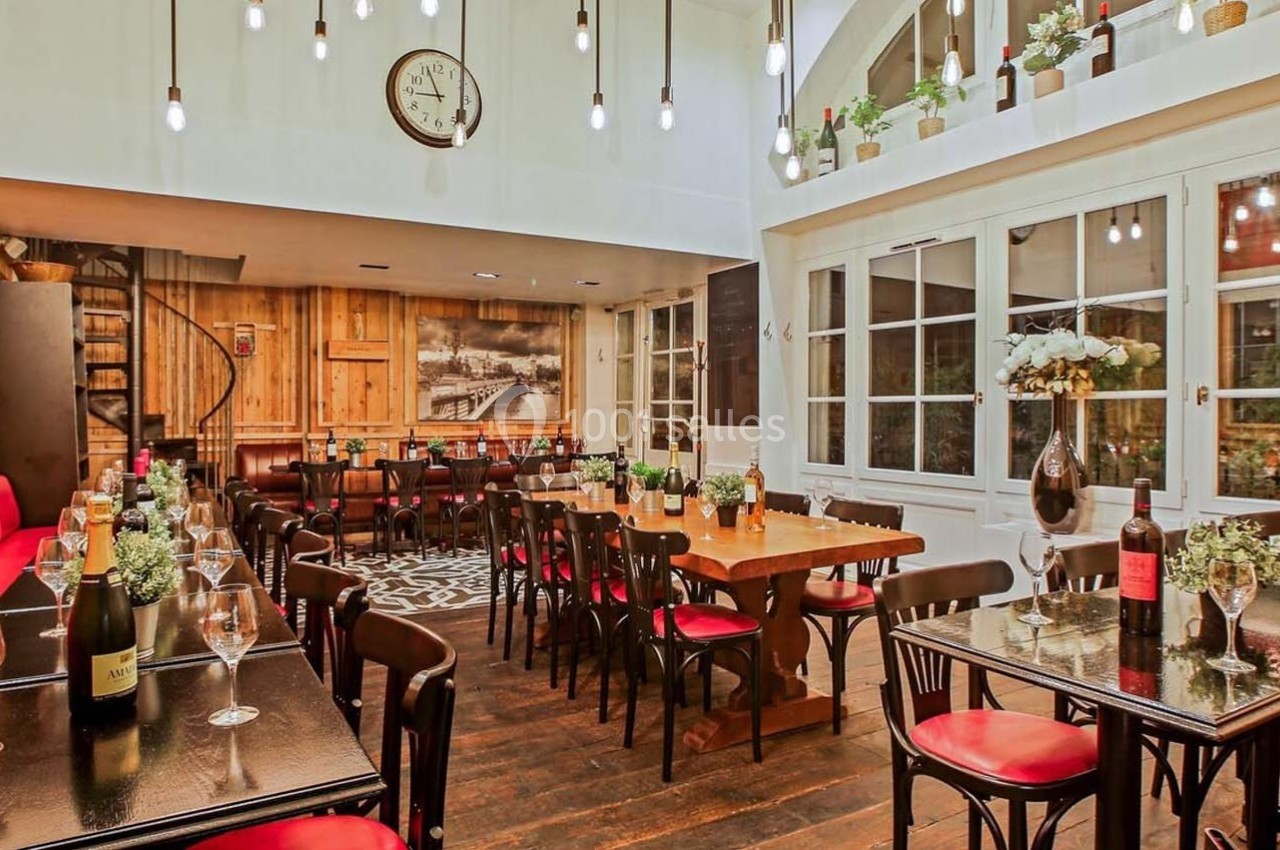 Salle de restaurant chaleureuse avec tables en bois, chaises noires, banquettes rouges et éclairage suspendu.