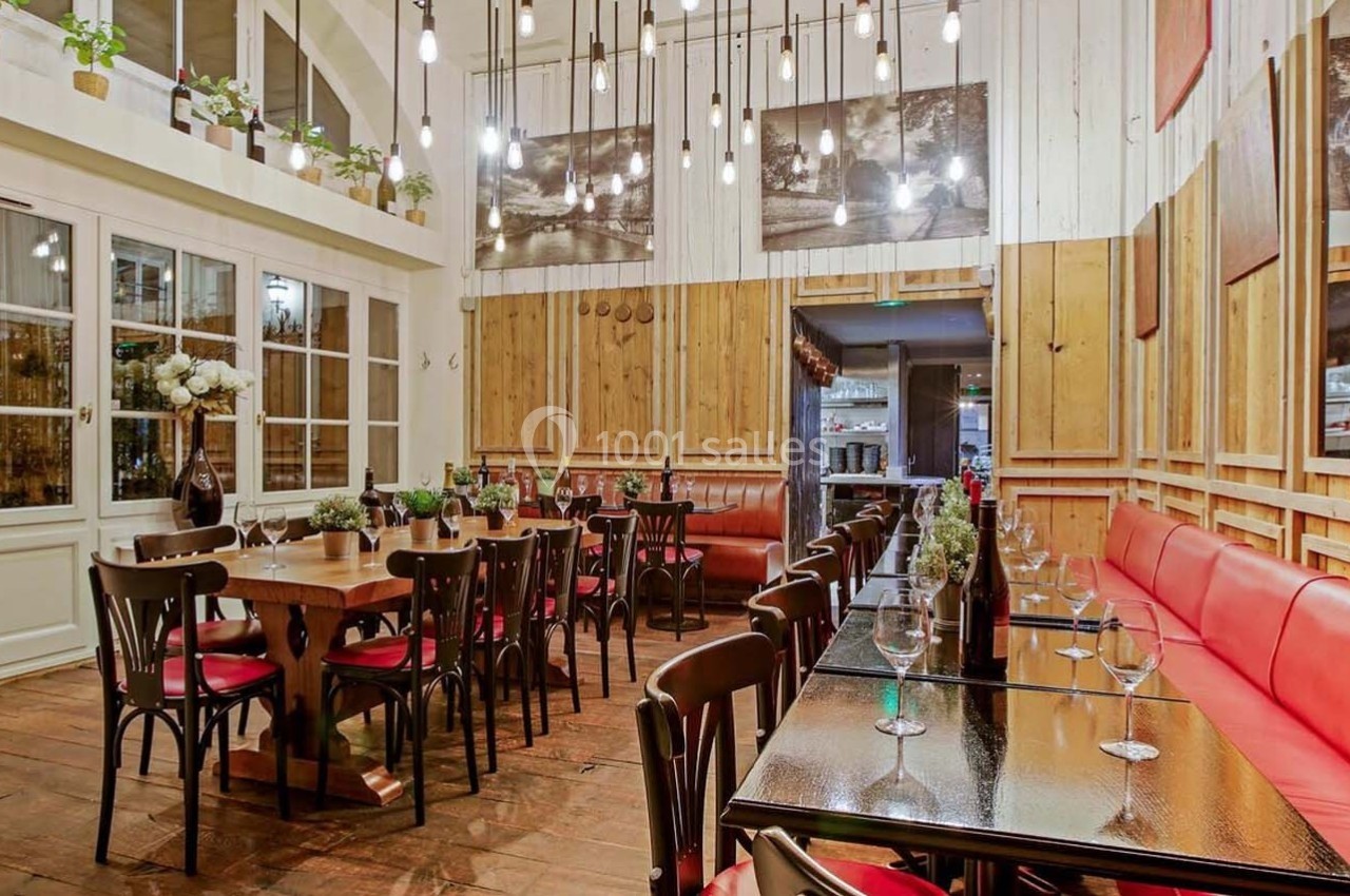 Salle de restaurant chaleureuse avec tables en bois, chaises noires, banquettes rouges et éclairage suspendu.