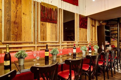 Salle de restaurant avec tables alignées, chaises noires, bouteilles de vin, plantes décoratives et murs en bois.