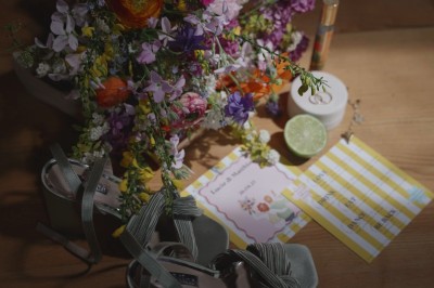 Bouquet de fleurs colorées, sandales vertes, lime coupée, bougie et carton imprimé sur une table en bois.