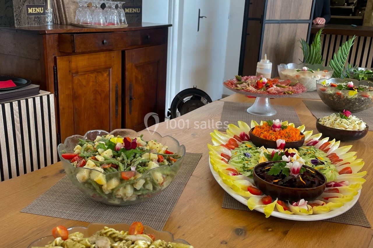 Buffet de plats variés comprenant des pâtes, salades et légumes, disposés sur une table en bois dans une salle lumineuse.