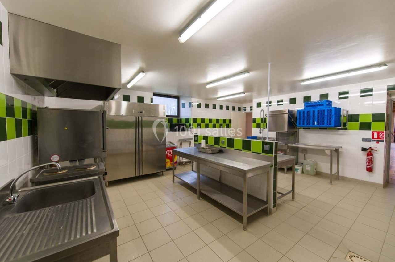 Cuisine professionnelle avec équipements en inox, carrelage blanc et vert, éclairage fluorescent et espaces de travail…