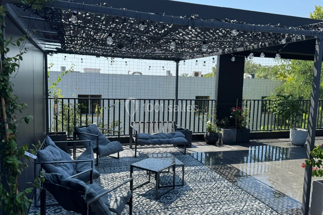 Terrasse moderne avec mobilier de jardin, pergola ombragée et sol en carreaux noirs et blancs, entourée de verdure.