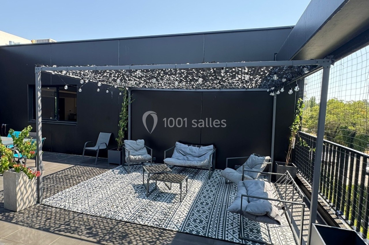 Terrasse aménagée avec pergola, tapis à motifs, fauteuils et coussins, entourée de plantes et de balustrades.