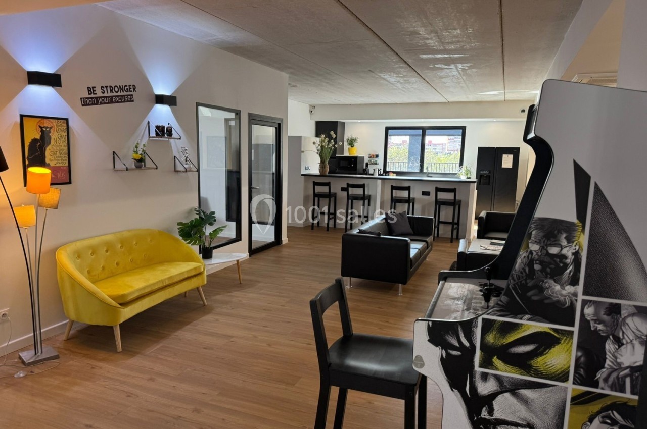 Espace intérieur moderne avec canapé jaune, coin détente, borne d'arcade et bar en arrière-plan.