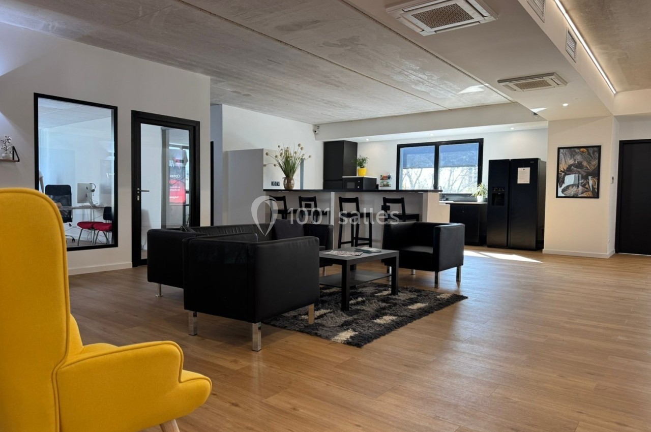 Espace de détente lumineux avec fauteuils, canapé, table basse, et cuisine ouverte en arrière-plan.
