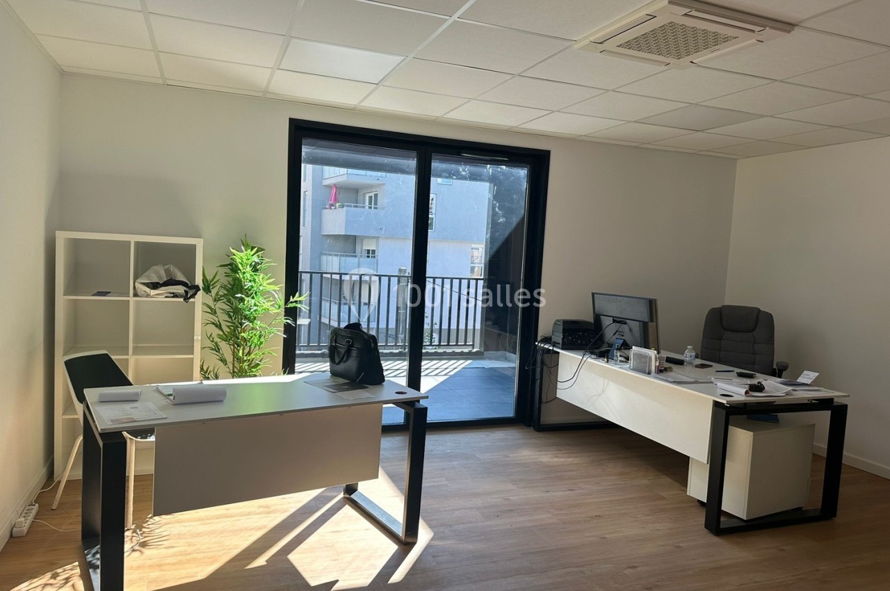 Bureau lumineux avec deux postes de travail, une plante verte et une baie vitrée donnant sur un balcon.