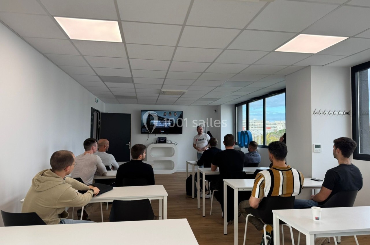 Un formateur s'adresse à un groupe de personnes assises dans une salle lumineuse équipée d'un écran.
