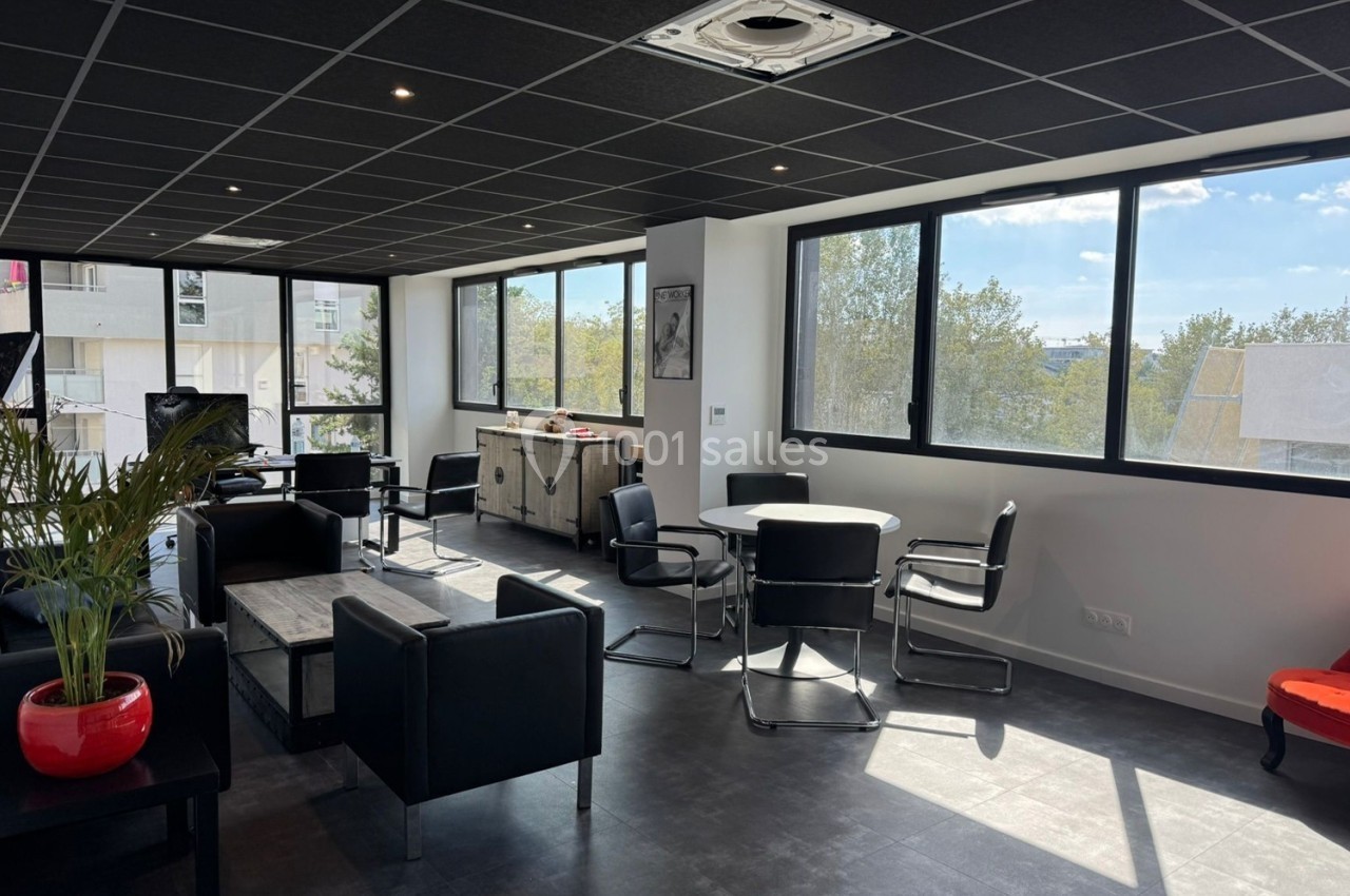 Espace de coworking lumineux avec mobilier moderne, grandes fenêtres et vue sur des arbres à l'extérieur.