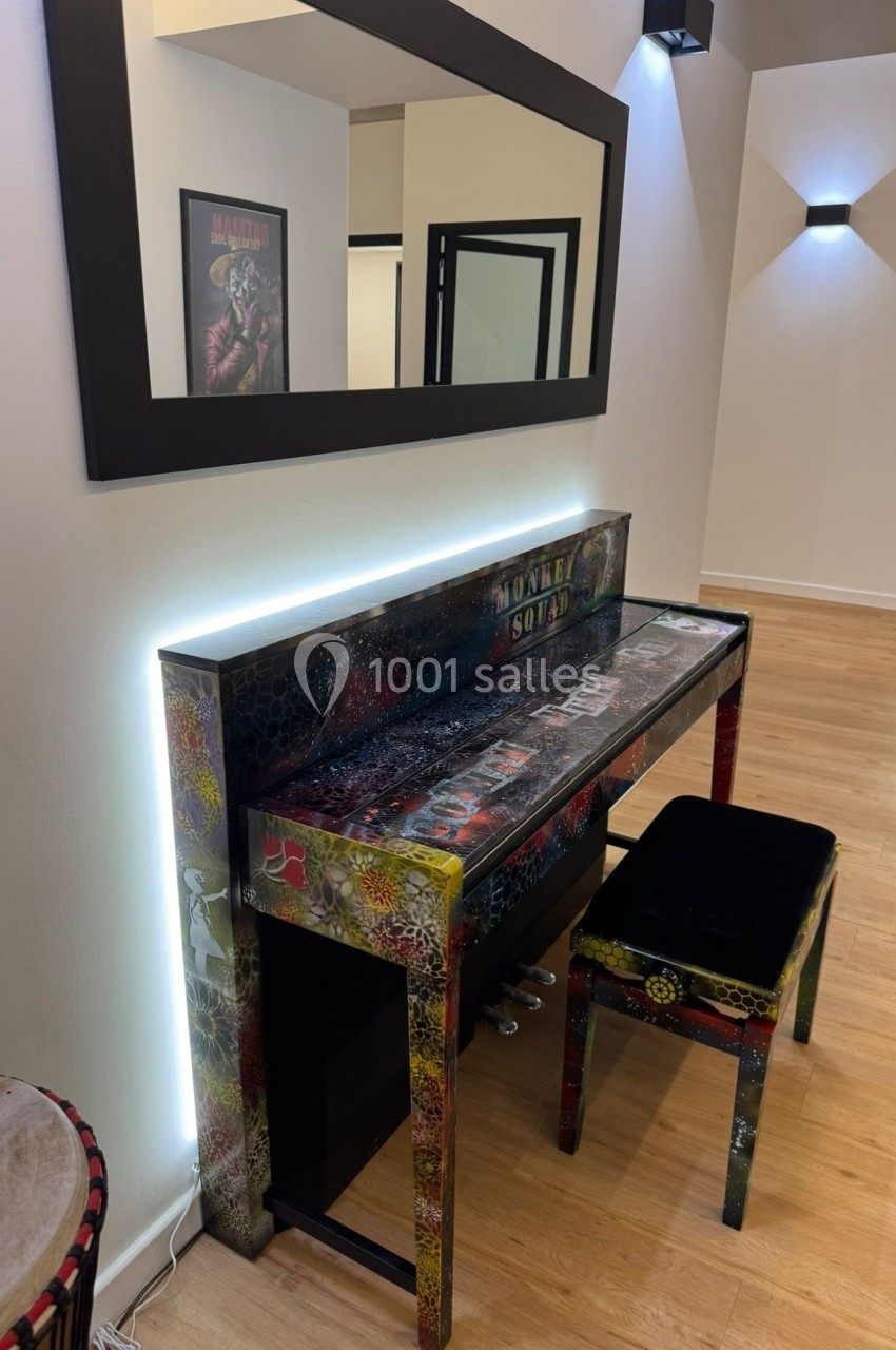 Piano droit coloré avec motifs artistiques, accompagné d'un tabouret noir, dans une pièce moderne au sol en bois.