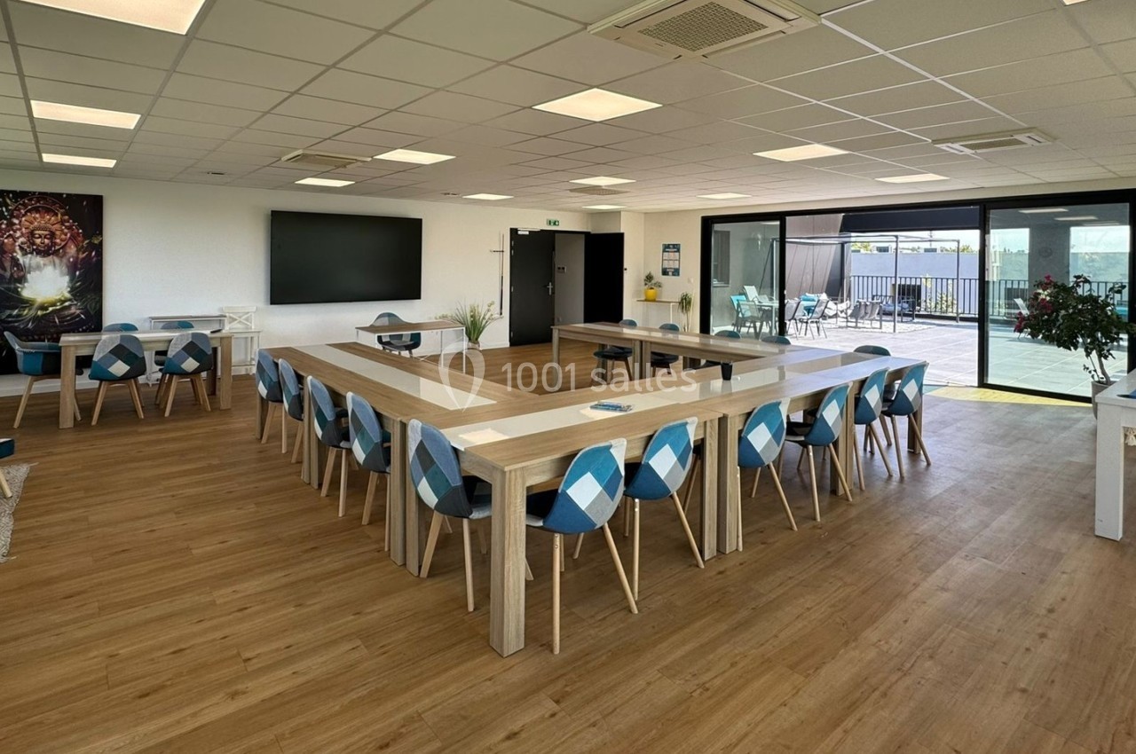 Salle lumineuse avec tables en bois disposées en U, chaises bleues, billard et accès à une terrasse extérieure.
