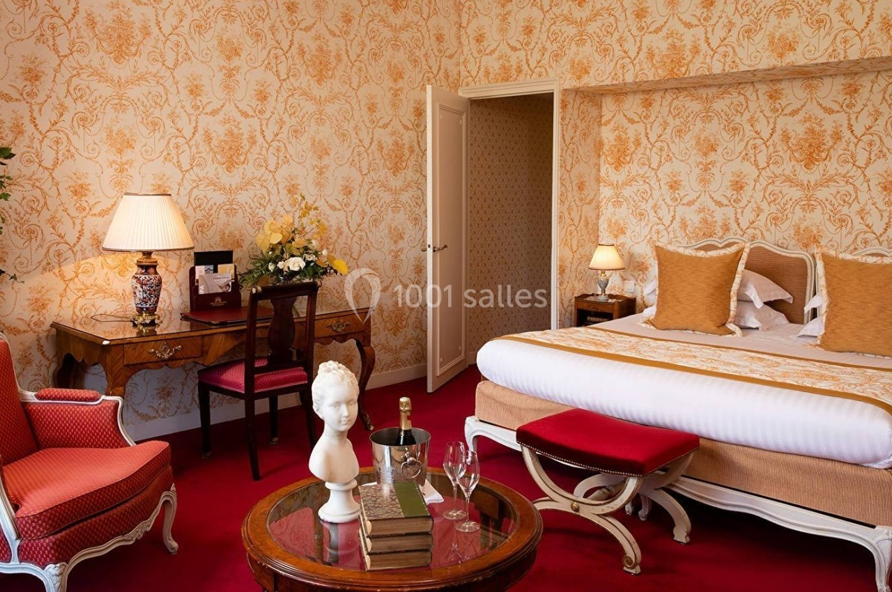 Chambre élégante avec lit double, mobilier classique, fauteuil rouge, bureau et décoration murale à motifs floraux.