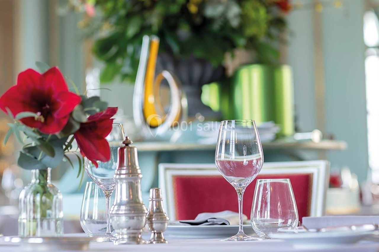Table dressée avec verres, carafe, fleurs rouges et salières, dans un restaurant élégant à la décoration raffinée.